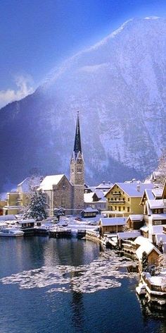 a snowy town with mountains in the background and snow covered buildings on the water's edge