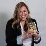 a woman holding a bag of food in one hand and smiling at the camera while wearing a black blazer