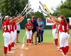 a group of women in red and white uniforms holding baseball bats on top of a field