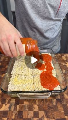 someone is adding sauce to some pasta in a glass dish on a wooden counter top