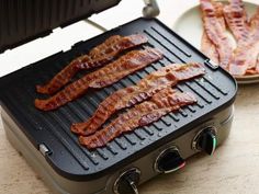 bacon is being cooked on the grill with two plates