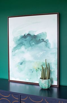 a painting is hanging on the wall above a blue dresser with a potted plant