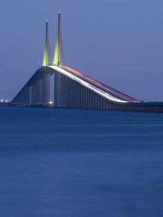 the bridge is lit up at night and it looks like it's going over water