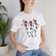 Comfort Colors® Dancing Skeleton Pumpkin T-shirt Celebrate the spooky season in style with our Retro Halloween Women's T-shirt! Featuring a playful design of dancing skeletons and a festive pumpkin, this tee is perfect for adding a touch of fun to your fall wardrobe. Whether you're headed to a Halloween party or just embracing the autumn vibes, this shirt combines comfort and humor for the ultimate seasonal look. Crafted from high-quality, soft fabric by Comfort Colors®, this T-shirt offers a re Halloween White Skull Top, White Skull Print T-shirt For Fall, White T-shirt With Skull Print For Fall, White Skull Print T-shirt For Halloween, Halloween Skull Print Crew Neck T-shirt, Fall Halloween Party, Pumpkin Tshirt, Skeleton Pumpkin, Funny Fall