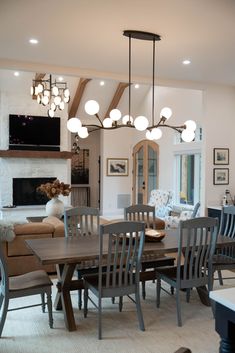 a dining room table and chairs with lights hanging from the ceiling above it in front of a fireplace