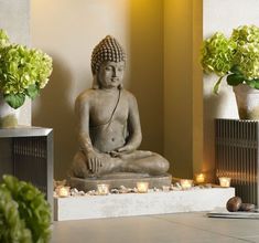 a buddha statue sitting on top of a table next to vases filled with flowers