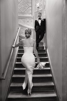 a woman in a white dress walking down stairs with a man in a tuxedo