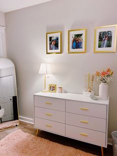 a white dresser sitting in a bedroom next to a wall with pictures and flowers on it