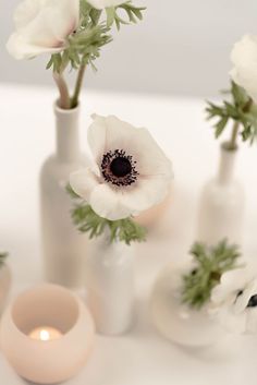 some white flowers are in vases on a table with one candle and the other two