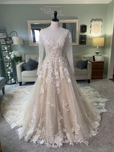 a wedding dress is displayed on a mannequin in front of a couch and mirror