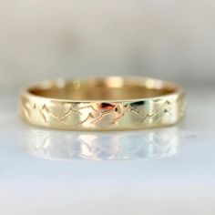 a gold wedding ring with horses on it's side, sitting on a white surface