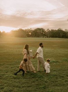 a man and woman holding hands while walking with two small children in a field at sunset