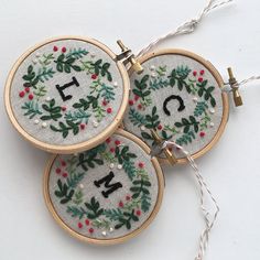 three embroidered christmas wreaths with numbers and holly leaves on them hanging from twine