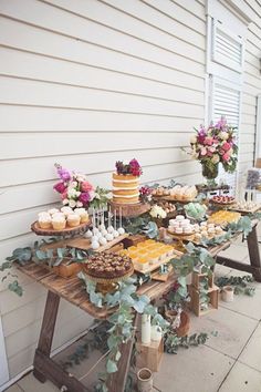 a table with cakes and cupcakes on it in front of a white house