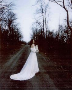 a woman in a long white dress standing on a road