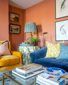 a living room with orange walls and blue couches in front of paintings on the wall