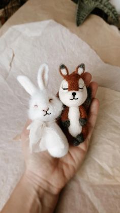 two small stuffed animals are held in someone's hand with tissue paper on the table