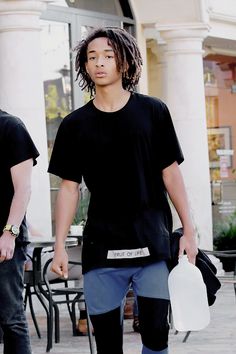 a young man with dreadlocks walking down the street carrying a white frisbee