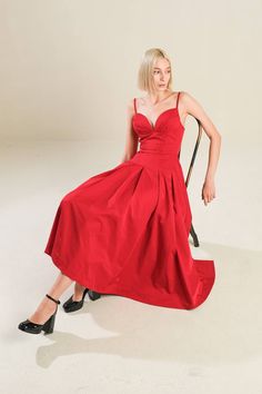 a woman in a red dress is sitting on a chair and posing for the camera