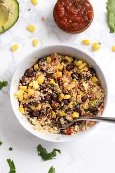 a bowl filled with rice, beans and corn next to an avocado on the side