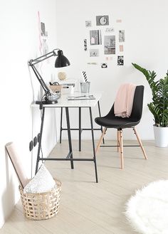 a room with white walls and wooden floors has a desk, chair, and potted plant in it