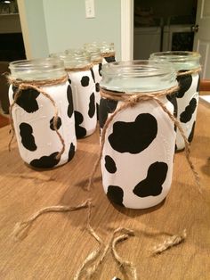 four mason jars with black and white cow print on them sitting on a wooden table