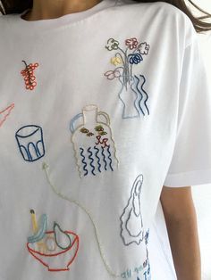 a woman wearing a white t - shirt with embroidered designs on it