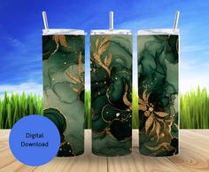 two green and gold tumblers sitting on top of a wooden table with grass in the background