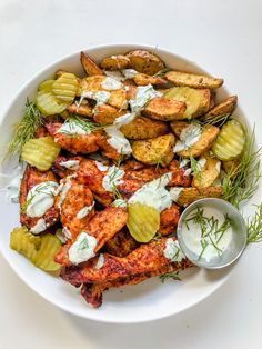 a white plate topped with chicken and potatoes covered in ranch dressing next to a small bowl of ranch dressing