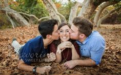 two people laying on the ground with leaves around them and one person kissing the other