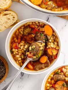 two bowls filled with soup next to bread on a white counter top and one bowl is full of stew