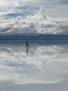 a person walking across a large body of water with clouds in the sky behind them