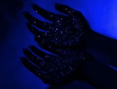 a person's hand with black glitter on it in the dark blue light,