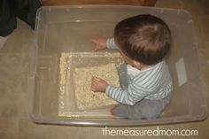 a toddler playing in a plastic container with food on the floor next to him