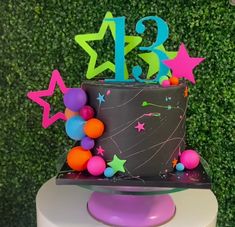 a birthday cake with stars and balloons on the top is decorated in black, purple, orange, and green