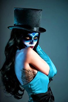 a woman with blue makeup and black hair wearing a top hat is posing for the camera