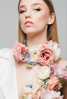 a woman with flowers on her neck wearing a white dress and pink lipstick is posing for the camera