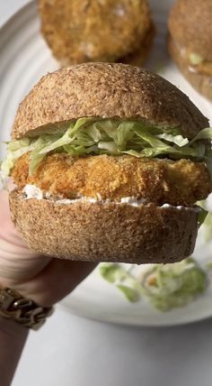 a hand holding a sandwich with lettuce and chicken on it next to some other food