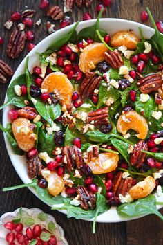 a salad with oranges, pecans and cranberries in a white bowl