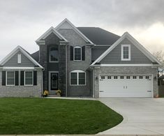 a large gray brick house with two garages and green grass in front of it