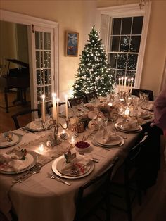 a dining room table set for christmas dinner with lit candles and plates on the table