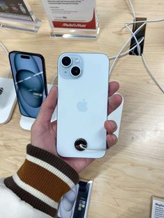 a person holding an iphone in front of two other cell phones on a wooden table