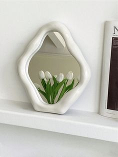 a vase with flowers in it sitting on a shelf next to a book and mirror