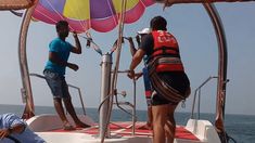 two people standing on the bow of a sailboat while another person is sitting down