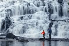 two people standing in front of a waterfall with water cascading down it's sides