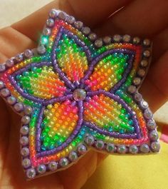 someone is holding a colorful beaded brooch in their hand and it looks like they are making something out of beads