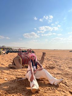 a woman sitting on top of a sandy beach next to a camel in the desert