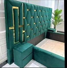 a bed with green velvet upholstered headboard and footstools in front of a potted plant