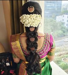 a woman with long hair wearing a green saree and flowers in her hair, looking out the window