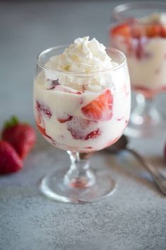 two desserts with strawberries and whipped cream in glasses on a table next to some strawberries